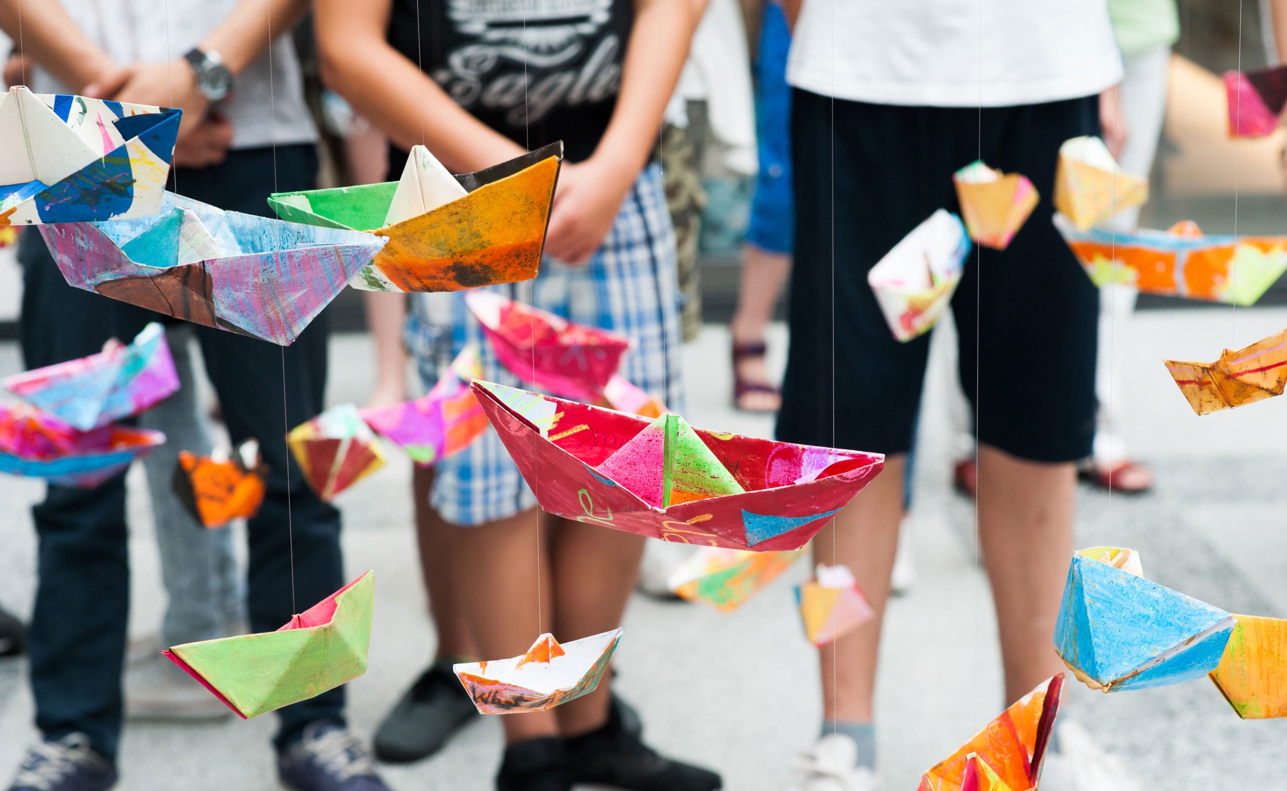 Children look at their colourful paper boats hanging on threads.